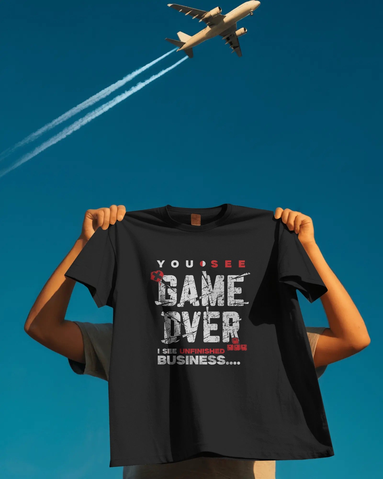 Person holding a black t-shirt with text in front of an airplane against a blue sky.